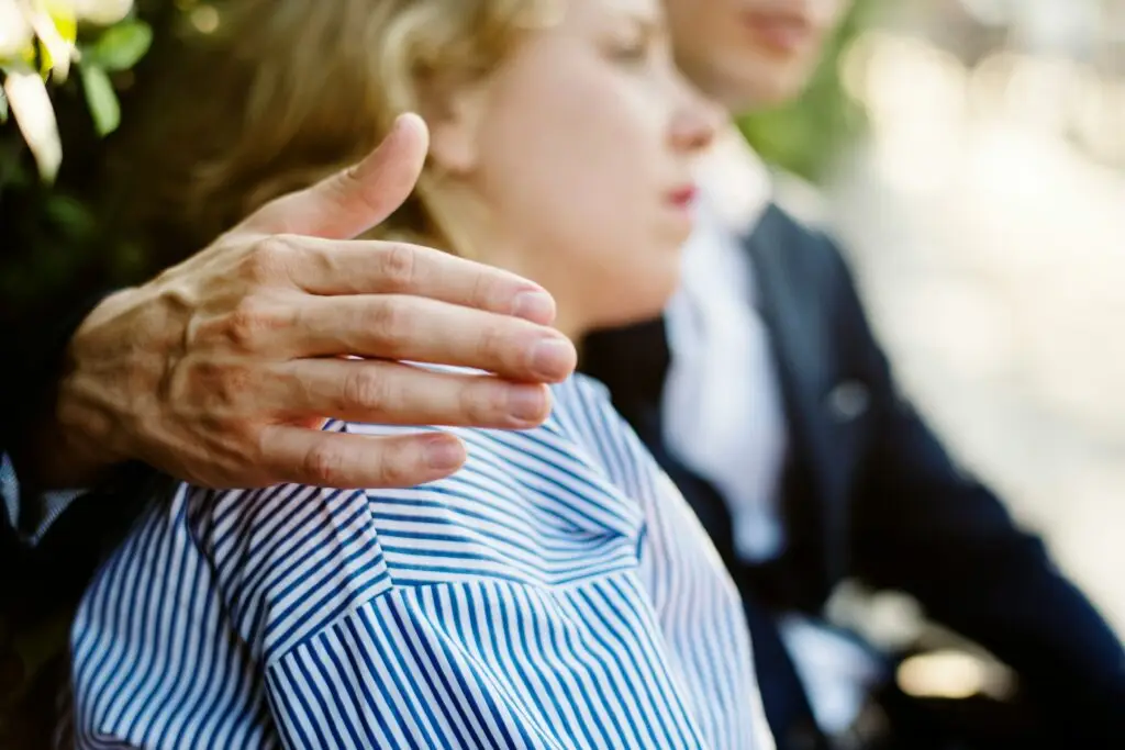 Hand resting on the shoulder of a woman sitting outdoors