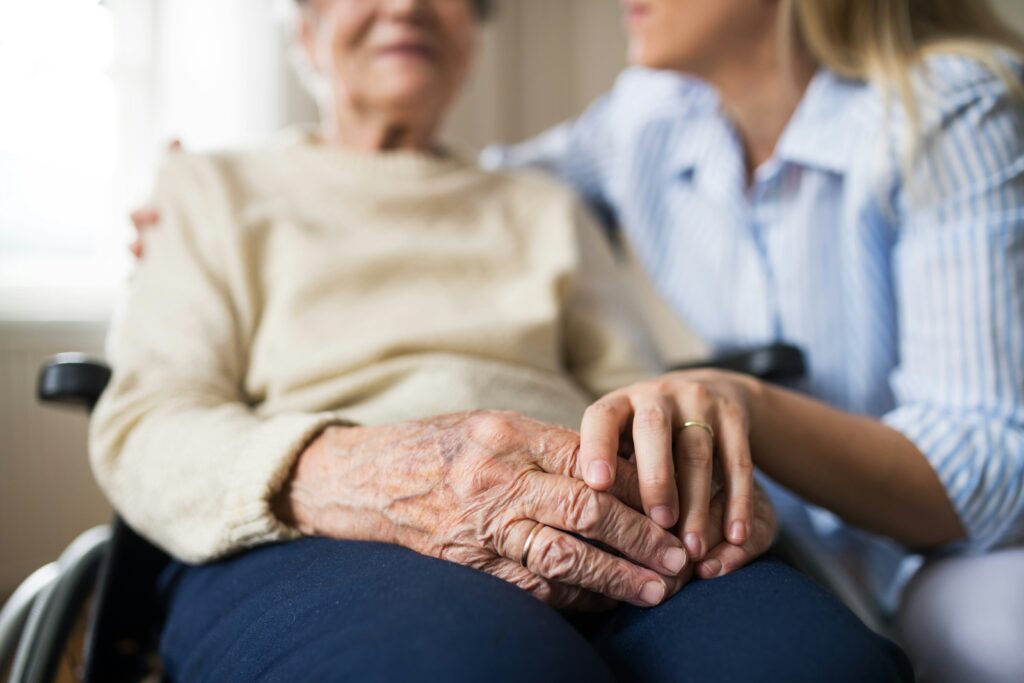A close-up of an elderly person in a wheelchair with a younger person gently holding their hand, showing care and support—reflecting the compassion at the heart of Minnesota elder law and life care planning. Only their hands and part of their faces are visible.