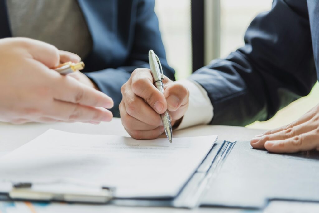 Close-up of two people in business attire at a desk, one signing a document while the other gestures, suggesting a discussion or agreement related to estate planning Minnesota.