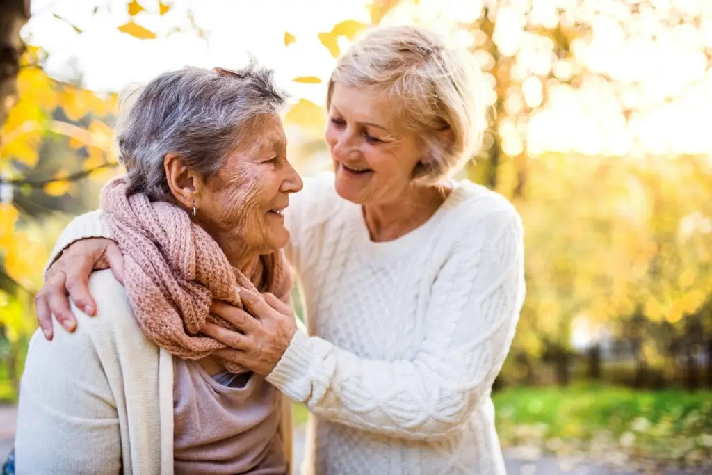 Two older women smiling at each other outdoors in autumn