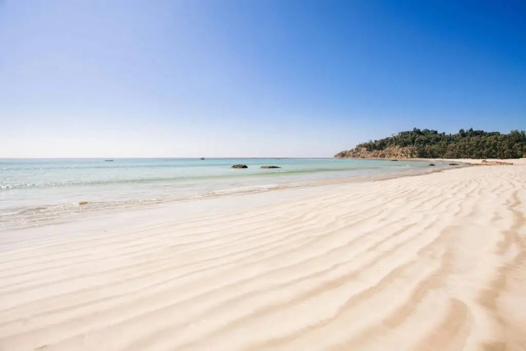 A serene beach with clear water and rippled sand under a bright blue sky.
