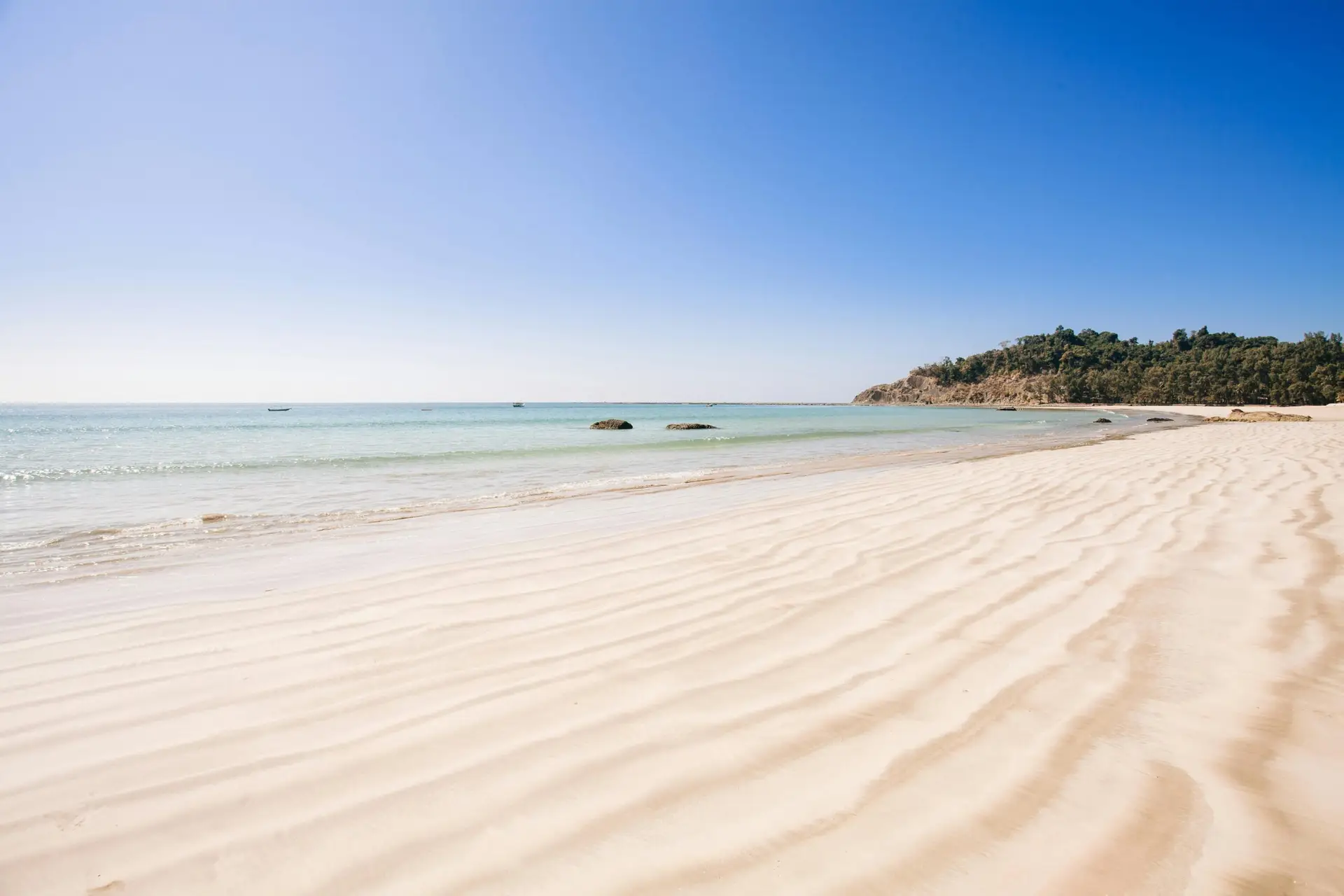 A serene beach with clear water and rippled sand under a bright blue sky.