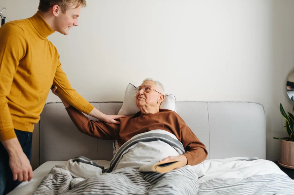 Young man checking on an older man resting in bed
