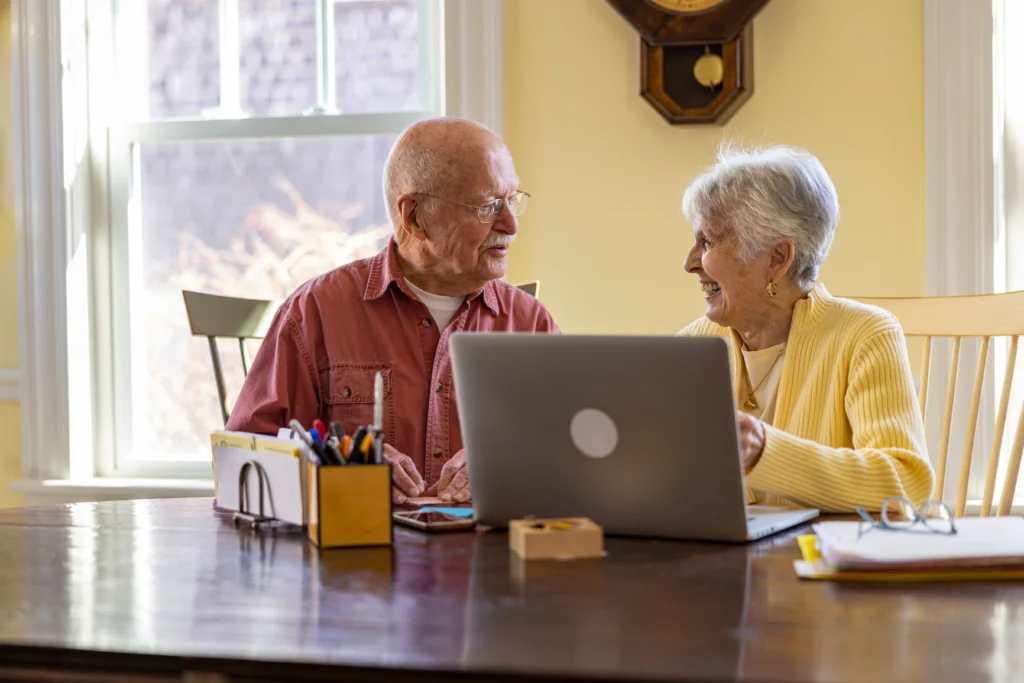 Older couple smiling at each other at a table with a laptop