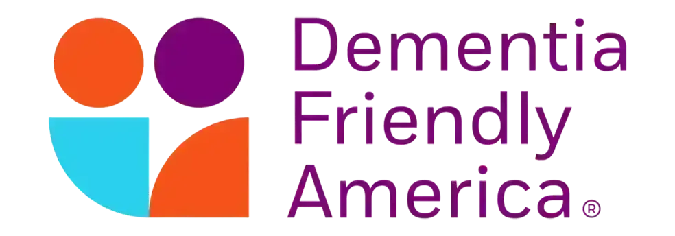 Logo for Dementia Friendly America. It features orange, purple, and blue abstract shapes on the left and the words Dementia Friendly America in bold purple text on the right, reflecting a supportive community for life care planning.