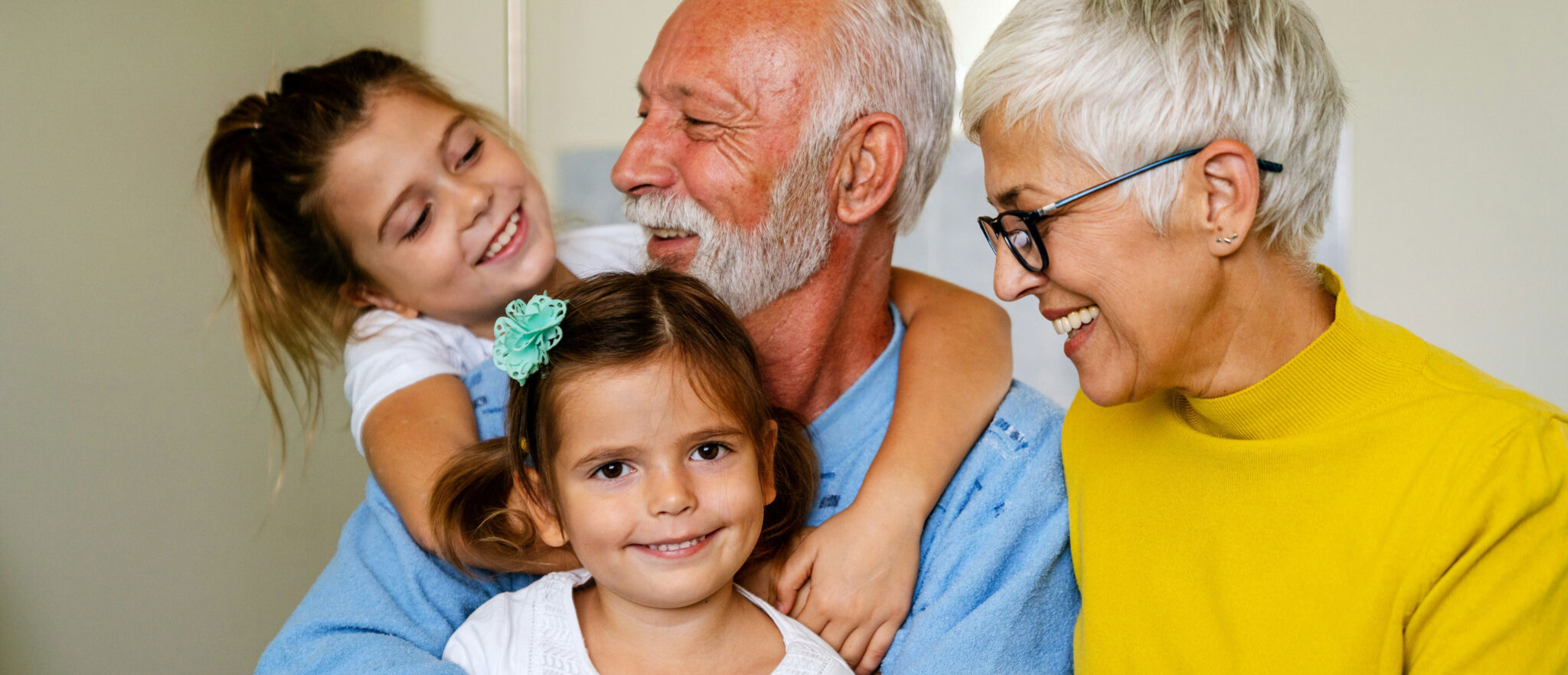 Two smiling grandparents sit with their two young granddaughters, sharing a joyful moment. This loving scene highlights the importance of Minnesota elder law and compassionate Medicaid planning for every generation.