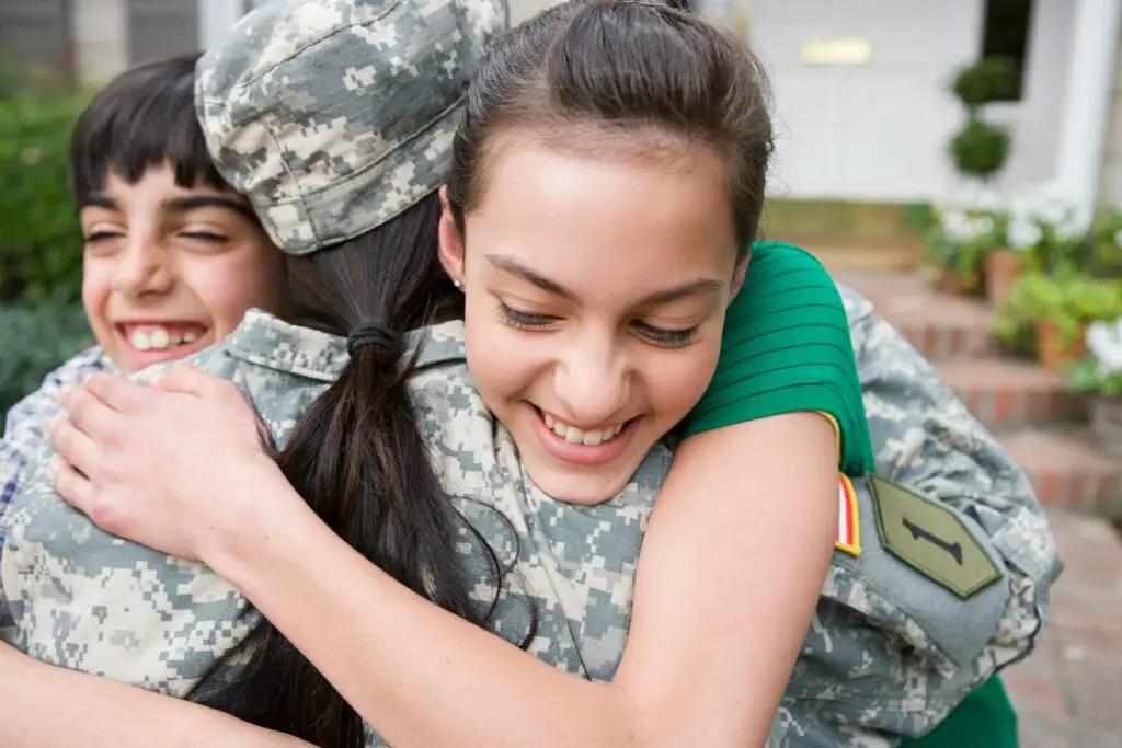 Two children hugging a person in military uniform outdoors