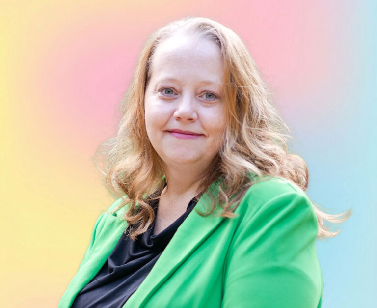 A woman with long, wavy blond hair wearing a bright green blazer and black top, smiling softly at the camera. The background is a smooth gradient of pastel pink, yellow, and blue—perfect for a Minnesota elder law or estate planning Minnesota profile.