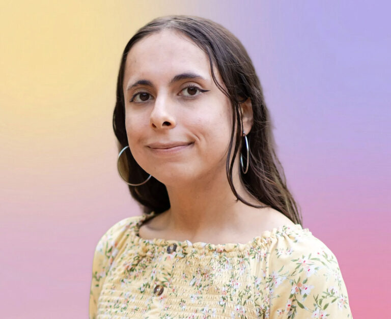 A person with long brown hair wearing large hoop earrings and a yellow floral top smiles slightly in front of a pastel gradient background, evoking the approachable style of an estate planning Minnesota professional.