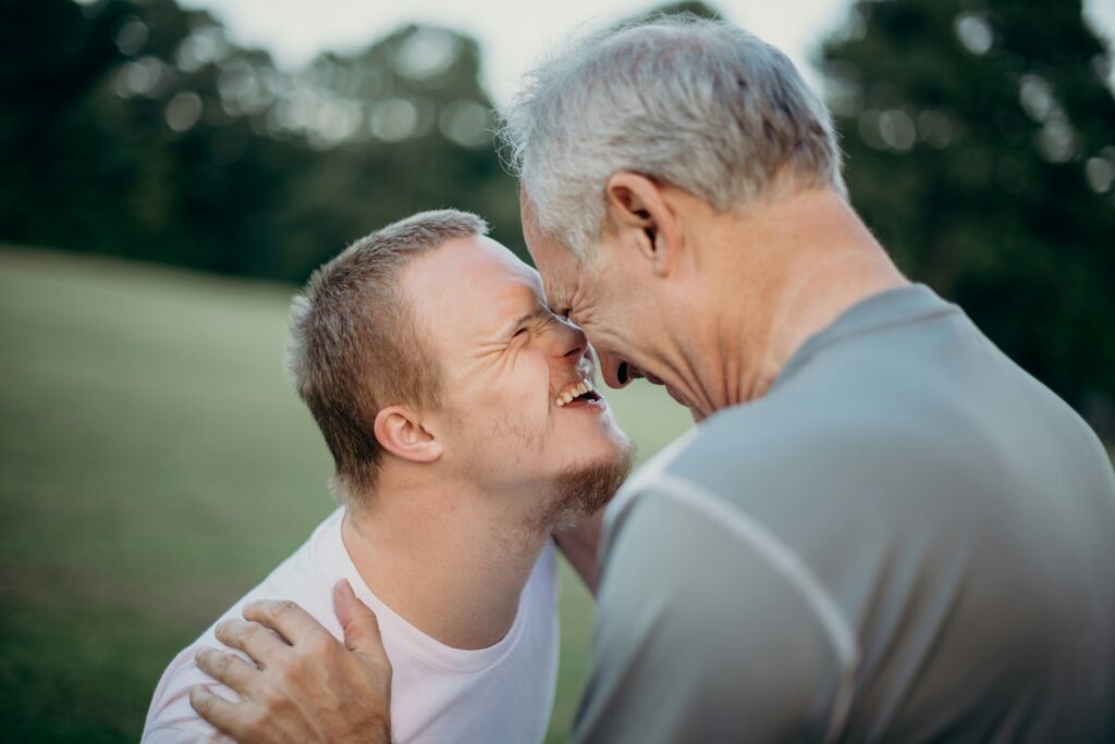 A young man with Down syndrome and an older man touch foreheads and smile warmly at each other outdoors, sharing a joyful and affectionate moment—a reminder of the importance of life care planning in the Twin Cities.
