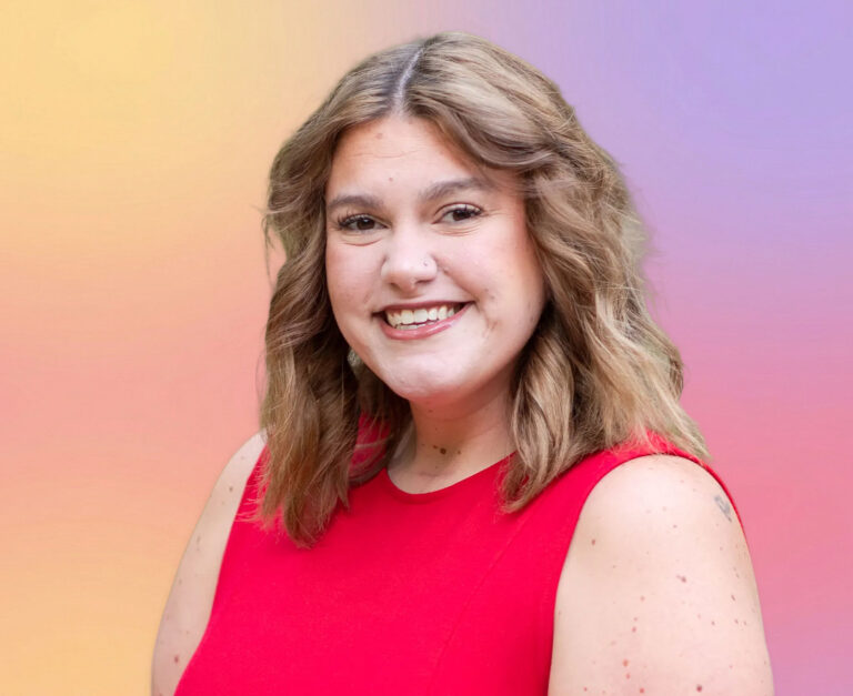 A woman with wavy, shoulder-length light brown hair smiles at the camera. She is wearing a sleeveless red top. The background is a soft gradient of yellow, orange, pink, and purple hues—perfect for a Minnesota elder law attorney’s profile photo.