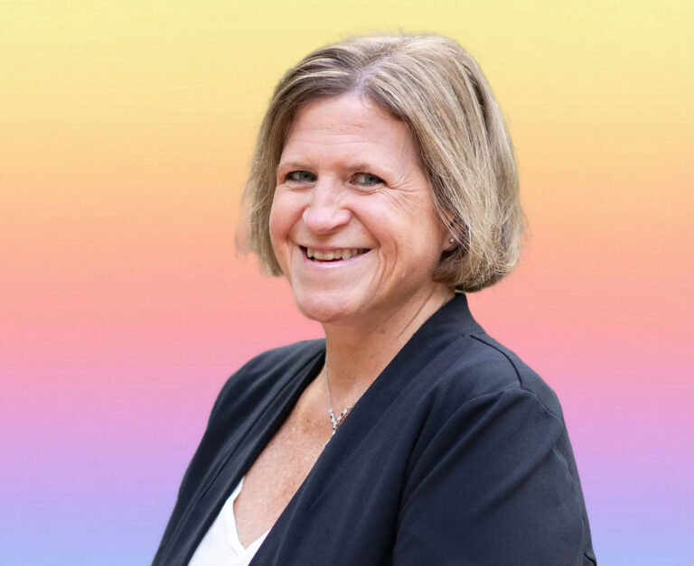 A smiling woman with short light brown hair wearing a dark blazer and white top stands in front of a soft gradient background, embodying the confidence of an elder law attorney experienced in estate planning Minnesota families trust.