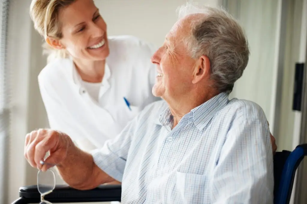 Caregiver smiling with an older man seated indoors