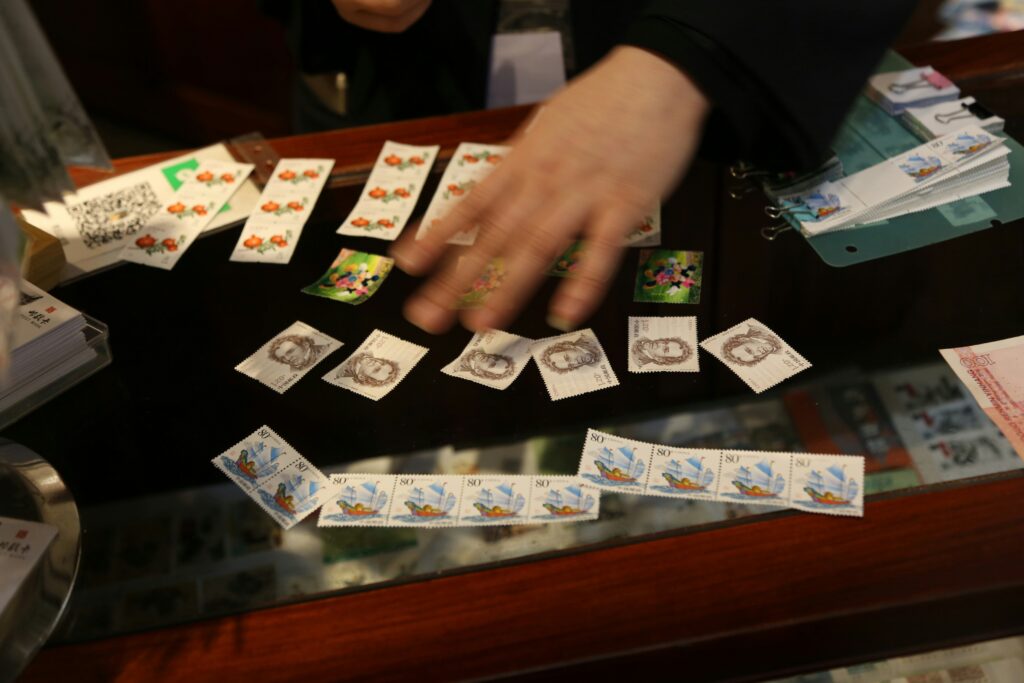 A person’s hand arranges collectible stamps and playing cards on a glass display counter in the Twin Cities. The colorful stamps and neatly laid-out cards reflect the charm of a Minnesota elder law enthusiast’s collection.