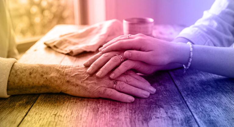 Two people sit at a wooden table, with a younger person gently holding and comforting the hands of an older person. The image, with its soft, warm, and colorful gradient overlay, reflects the compassionate guidance of Everbright Legacy Law.