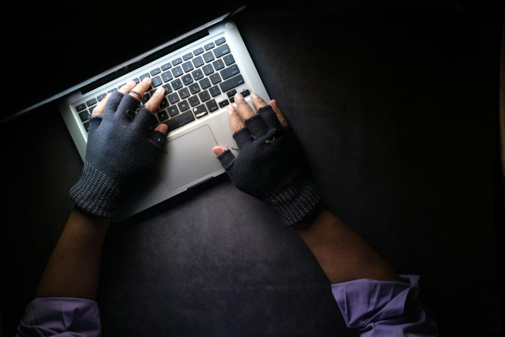 A person wearing fingerless gloves types on a laptop keyboard in a dimly lit environment, with their hands and part of a purple sleeve visible—capturing the tense moment as they investigate tech support scams or suspicious pop-up alerts.
