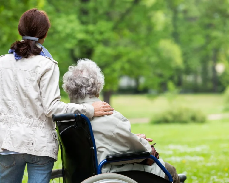 Woman resting her hand on the shoulder of an older woman in a wheelchair in a park