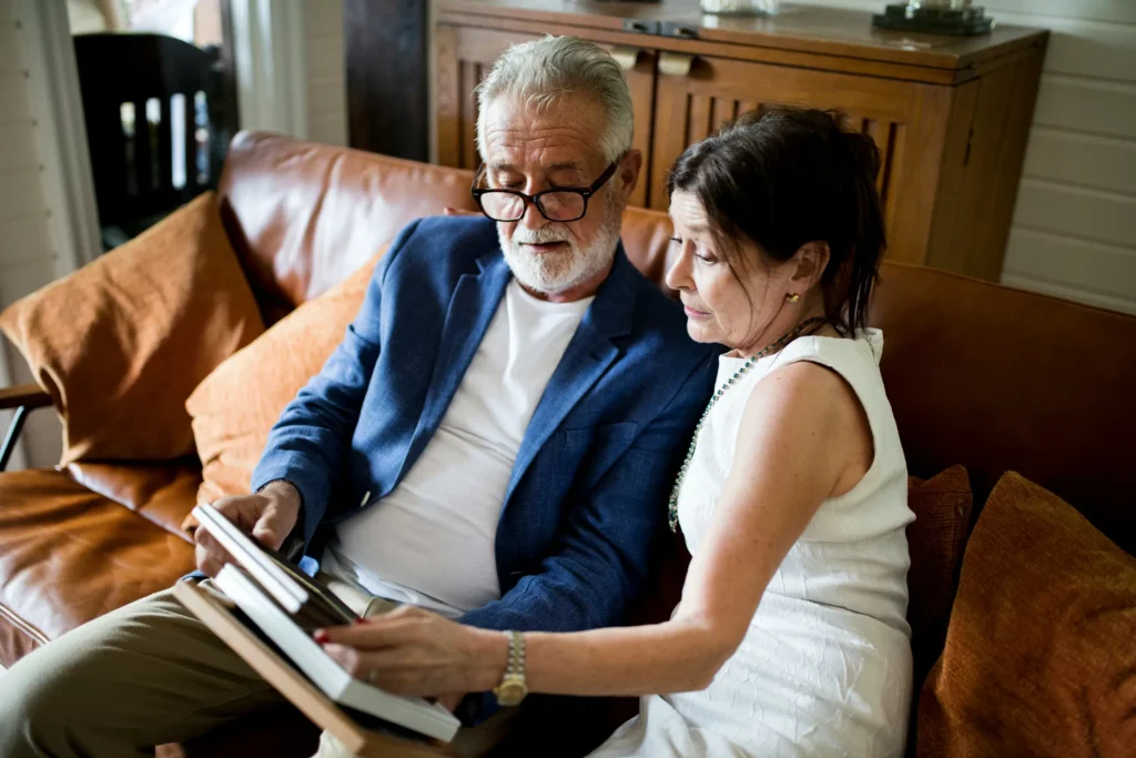 Older couple on a leather sofa reading through papers and a tablet together