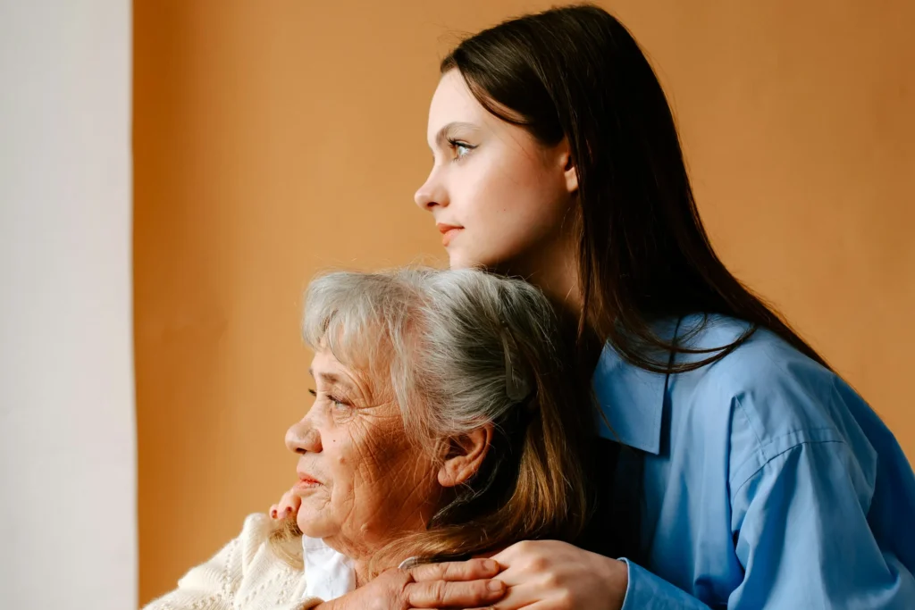 Adult daughter in a blue shirt hugging her older mother from behind