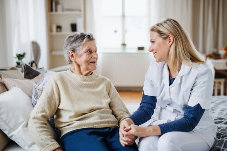 Caregiver in a white uniform holding hands with a smiling older woman