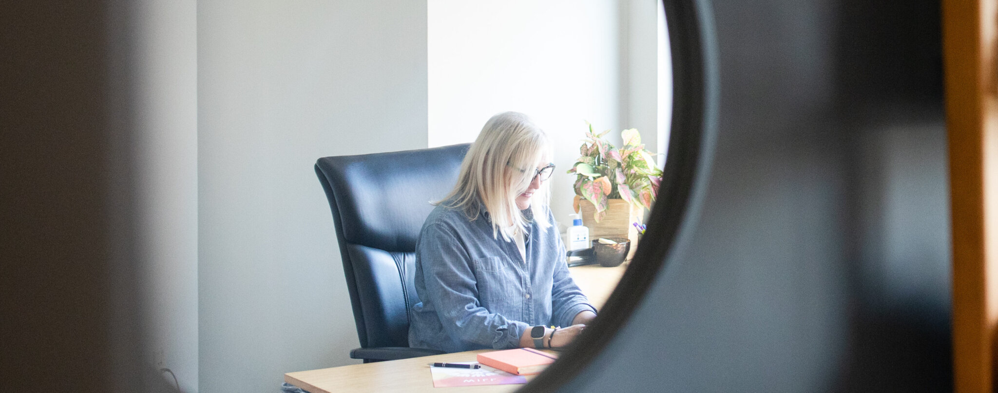 Sarah Sicheneder, Founder, Attorney at Law, working at her desk, seen through a round mirror