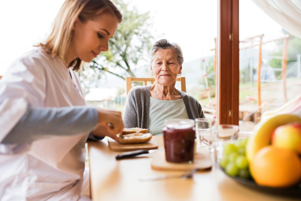 A young woman prepares food for an older woman at a table with fruit, jam, and drinks. As they sit indoors near a large window with trees visible outside, their conversation turns to estate planning and how thoughtful decisions today can help secure a lasting legacy for generations to come.