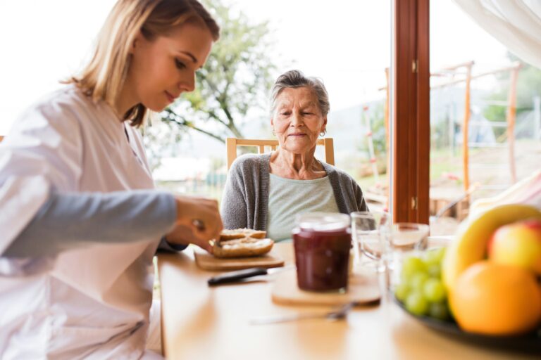 A young woman prepares food for an older woman at a table with fruit, jam, and drinks. As they sit indoors near a large window with trees visible outside, their conversation turns to estate planning and how thoughtful decisions today can help secure a lasting legacy for generations to come.