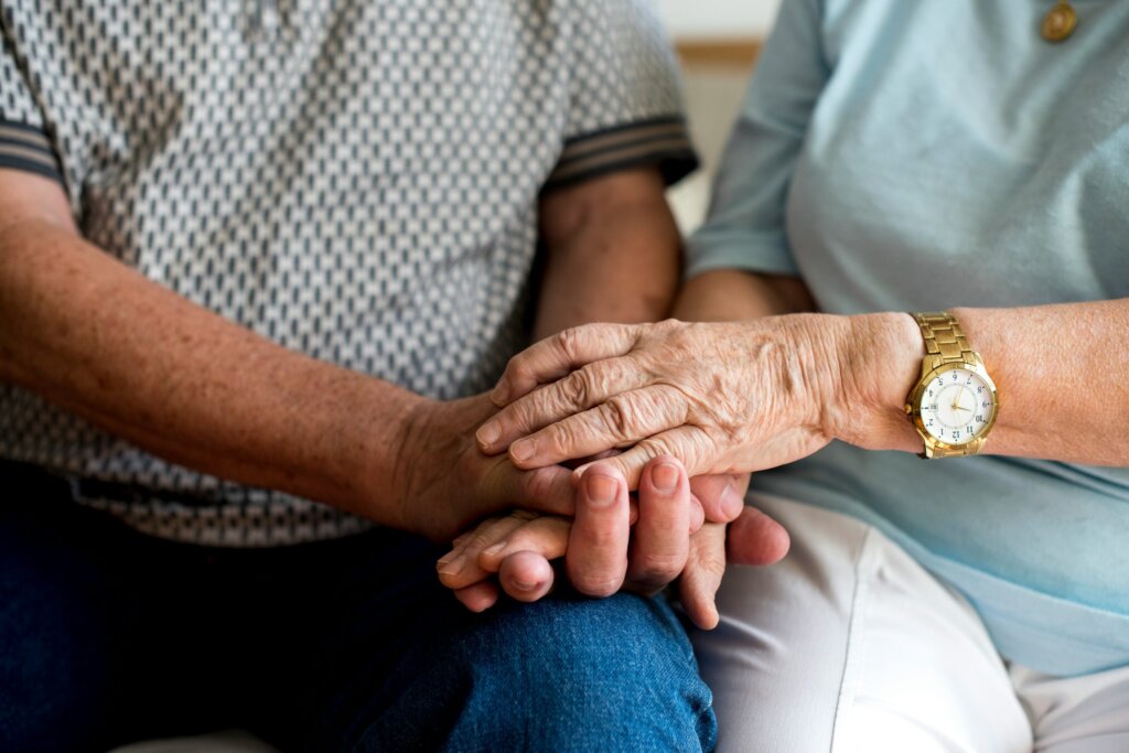 An older couple holding hands while seated side by side